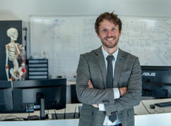 Brian Horsak steht mit verschränkten Armen vor seinem Arbeitsplatz