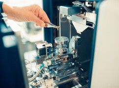 Eine Hand setzt mit einer Pinzette einen Teil in ein Gerät der Core Facility...