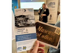 Der Folder und eine Karte mit dem App Hinweis werden vor die Kamera gehalten