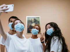 Studierende mit Mundschutz lächeln in Kamera und machen ein Selfie