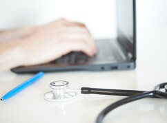 Medizinstudent tippt am Laptop Daten ein neben ihm liegt ein Stethoskop