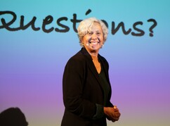 Una-May O'Reilly auf der Bühne mit dem Text Questions im Hintergrund