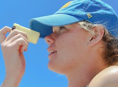 Eine hellhäutige Frau trägt eine Kappe und cremt ihre Nase ein