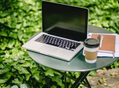 Büroarbeitsplatz im Grünen mit Laptop, Notizen und Kaffee